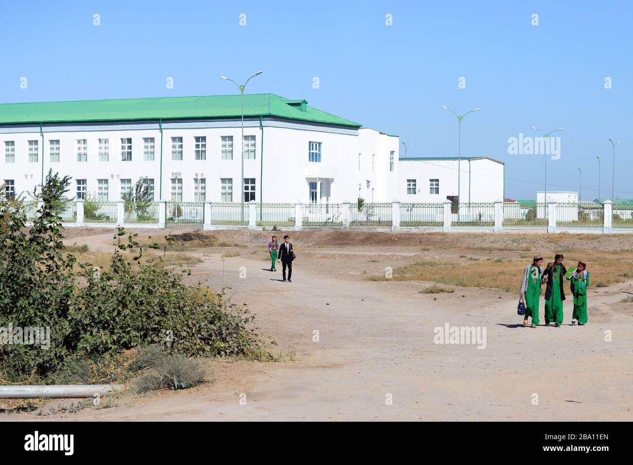 Turkmen school white building with green roof. Local students walking with tradition clothes, the national dress for girls. Dashoguz, Turkmenistan. Stock Photo