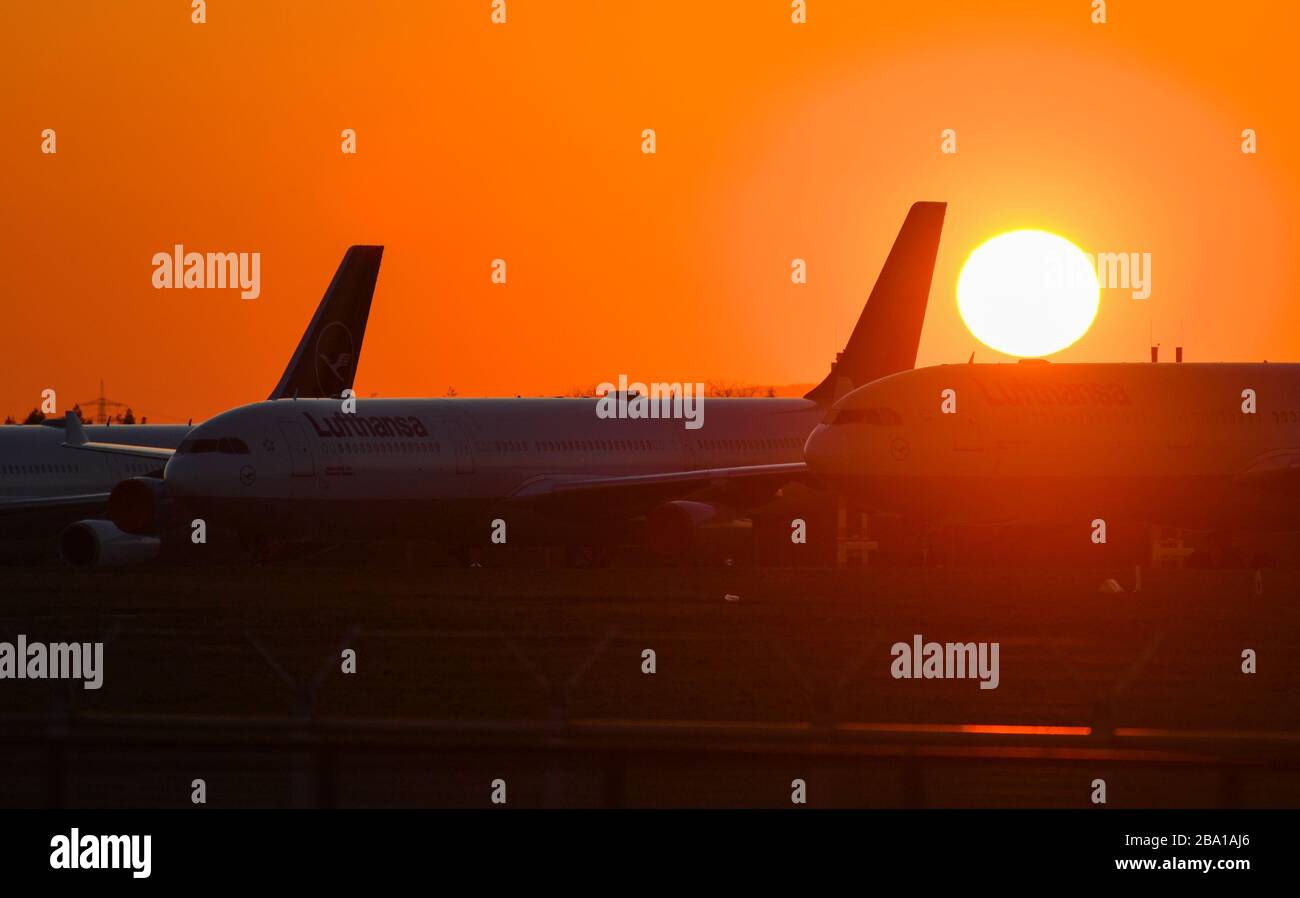 25 March 2020, Hessen, Frankfurt/Main: The sun sets behind Lufthansa passenger planes standing on the closed runway northwest of Frankfurt Airport. Lufthansa parked jets not needed during the Corona crisis there. Photo: Arne Dedert/dpa Stock Photo