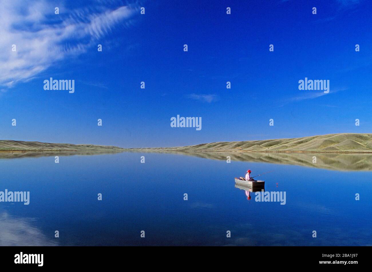 A man fishing in a boat  on the tranquil water of McGregor Lake, Alberta Canada Stock Photo