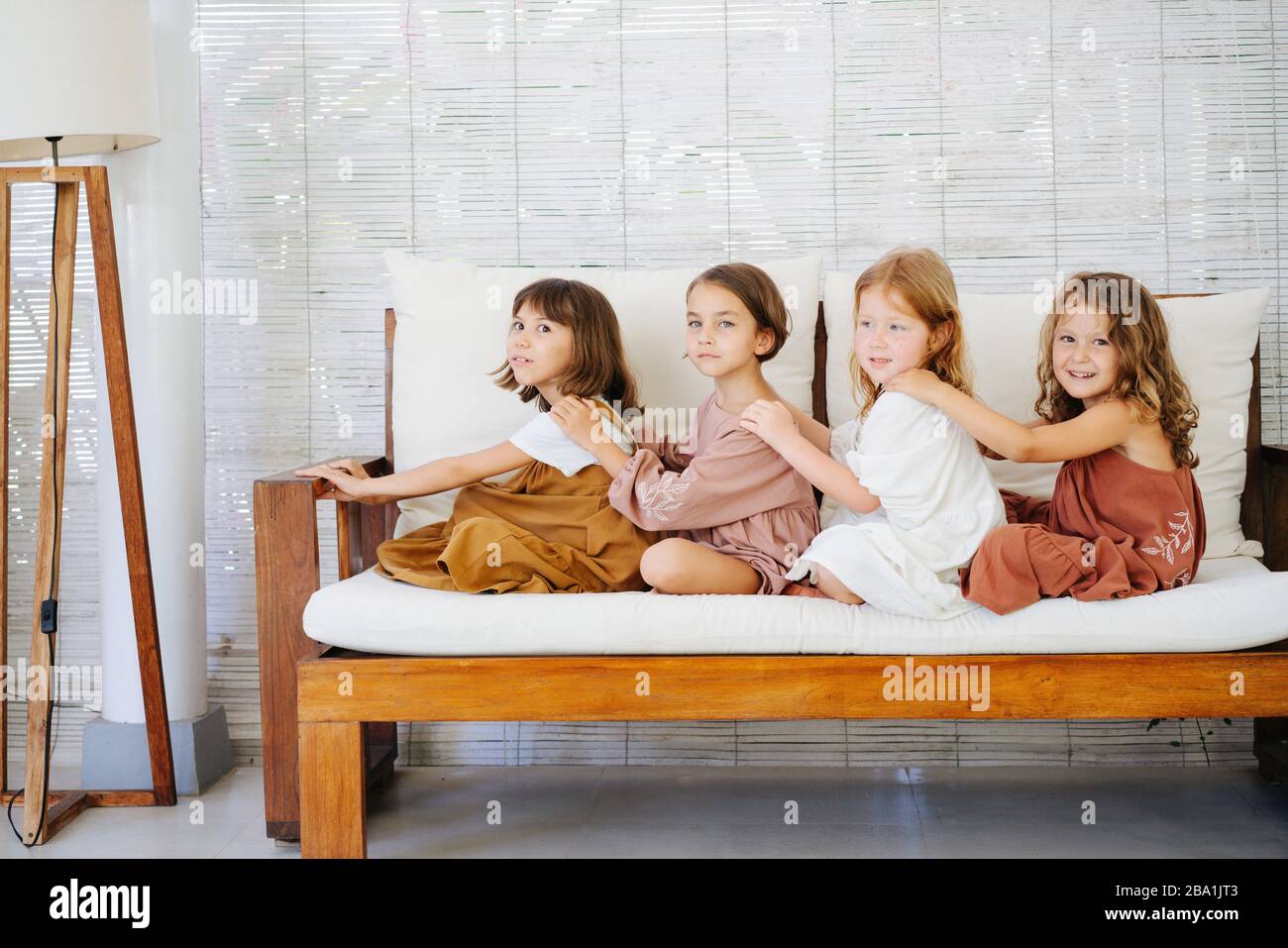 Four little girls sitting in a row on a sofa one behind another Stock