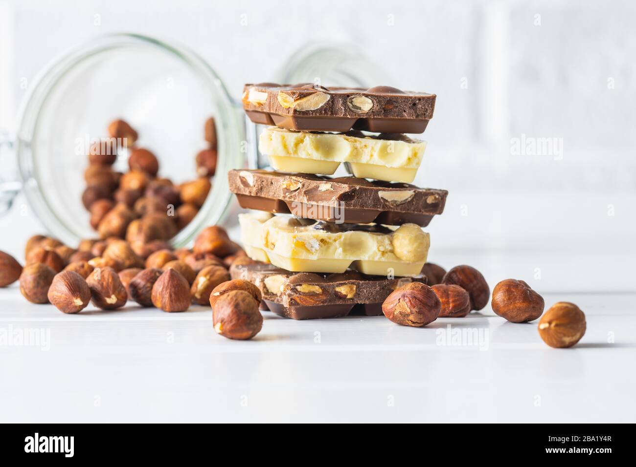 White and dark nut chocolate with hazelnuts on white table. Stock Photo