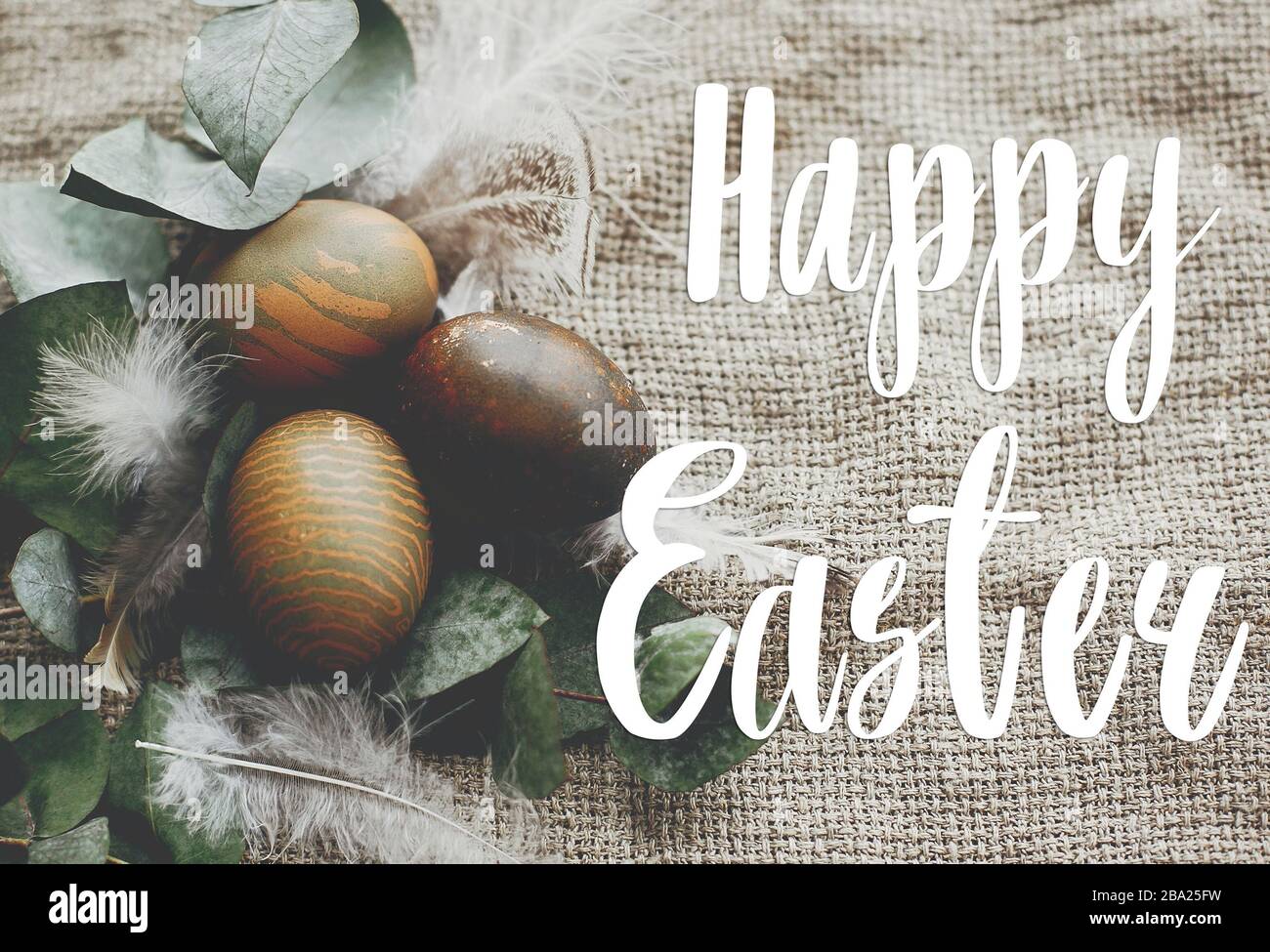 Happy Easter text. Easter greetings card. Stylish easter eggs with feathers on rustic table. Natural dyed green easter eggs with eucalyptus branch, sp Stock Photo