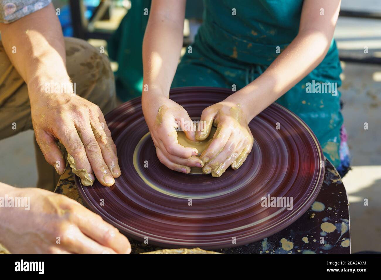 Master and student. Childrens hands in the yellow clay on the rotating Potters wheel molded the dishes. Craft Stock Photo