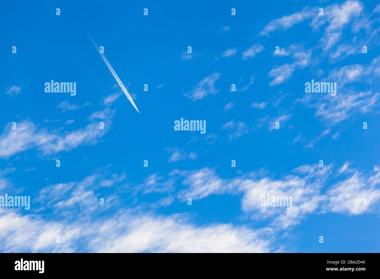 Airplane contrail high up at blue sky at flight between clouds (copy space) Stock Photo