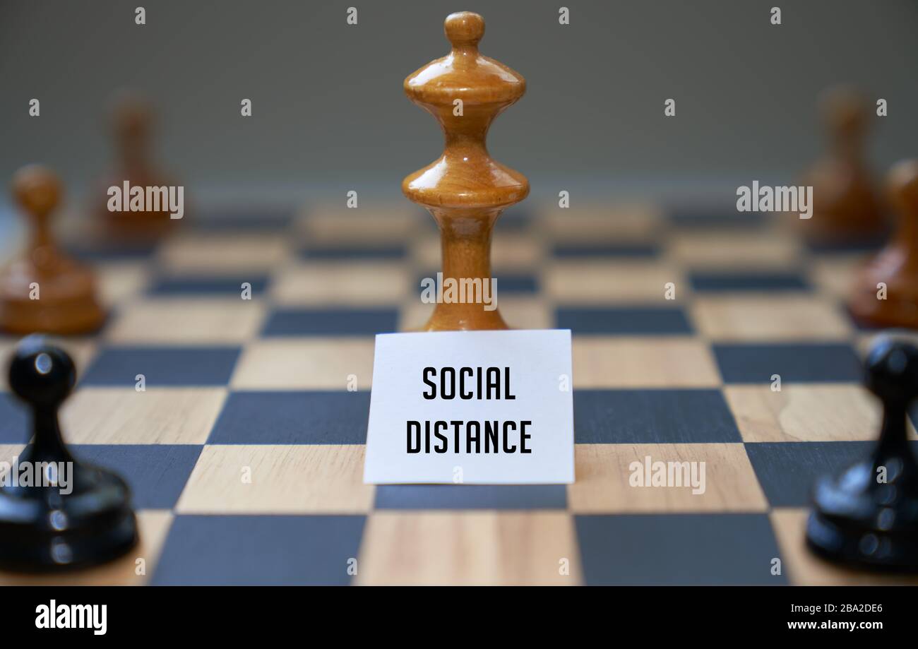 Concept chess pieces express social distancing with white board and text social distance in front of the center piece on the chess board. Stock Photo