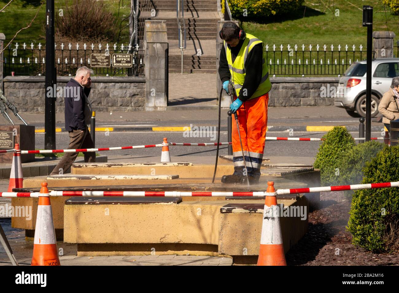 Council worker with pressure washer hose cleaning street benches on sunny day as Springtime cleaning on streets of Killarney, County Kerry, Ireland Stock Photo