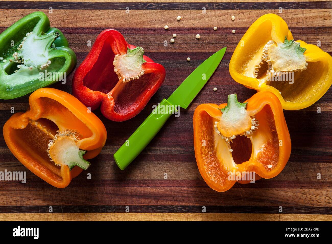 yellow, orange green and red bell peppers with paring knife on a wooden cutting board Stock Photo