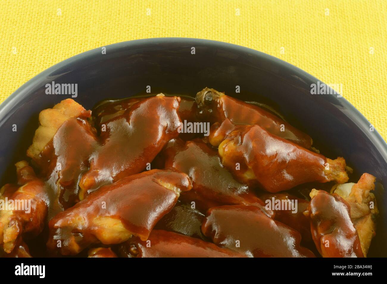 Close up of chicken wings with barbecue sauce in blue bowl against yellow tablecloth Stock Photo