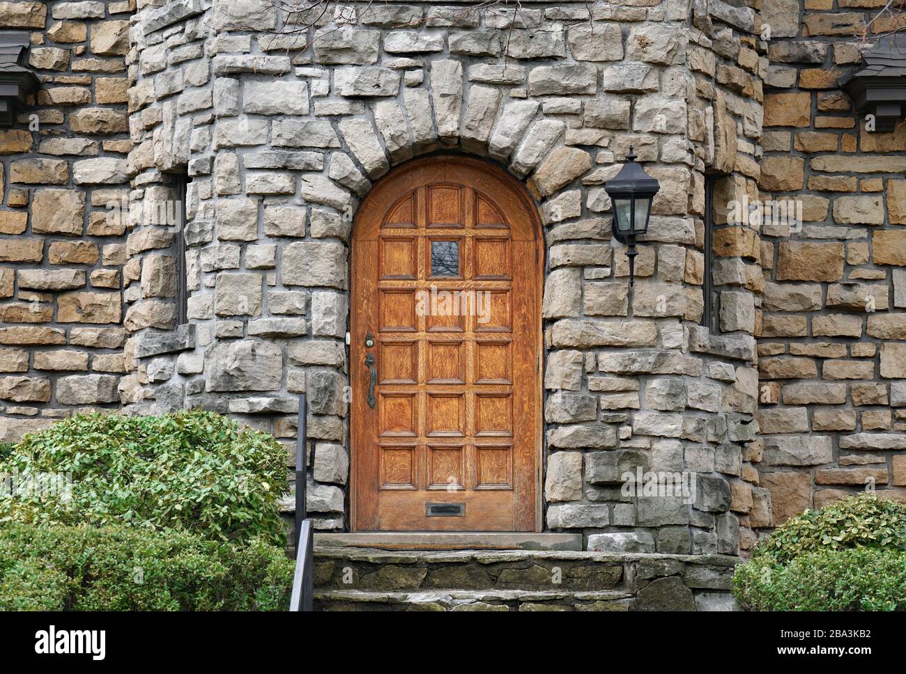 Round top wood panel door of house built of rough hewn stone Stock Photo