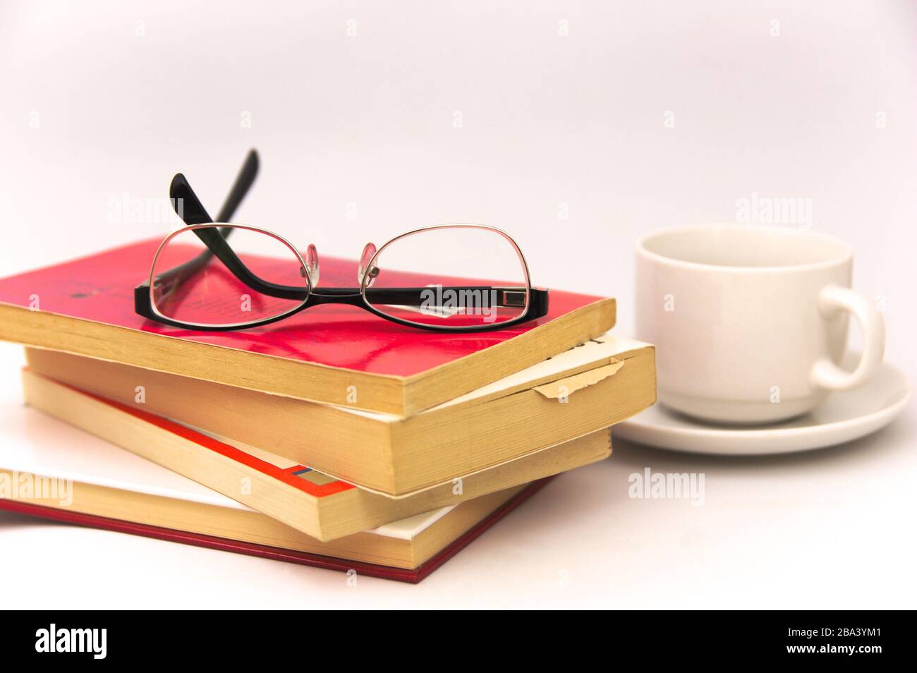 Image of some books on which there are reading glasses next to an infusion cup all isolated on white background Stock Photo