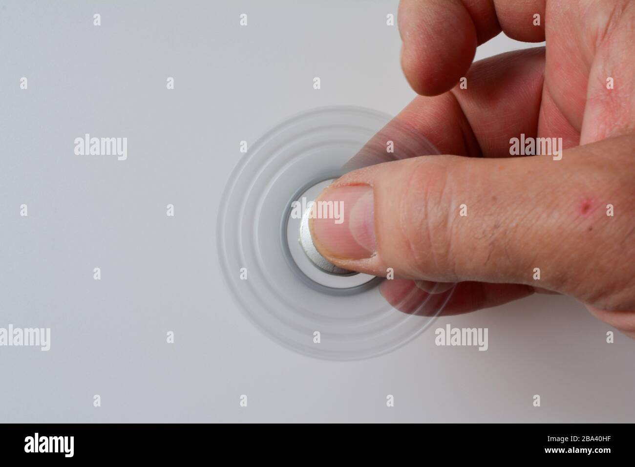 Silver fidget spinner in motion in man's hand over white background, copy space on left Stock Photo