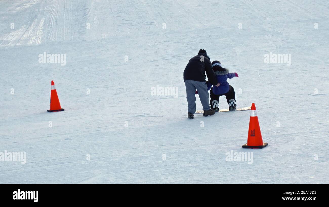 Father helping a young girl to learn to play snowboard in winter, outside, healthy lifestyle. Stock Photo