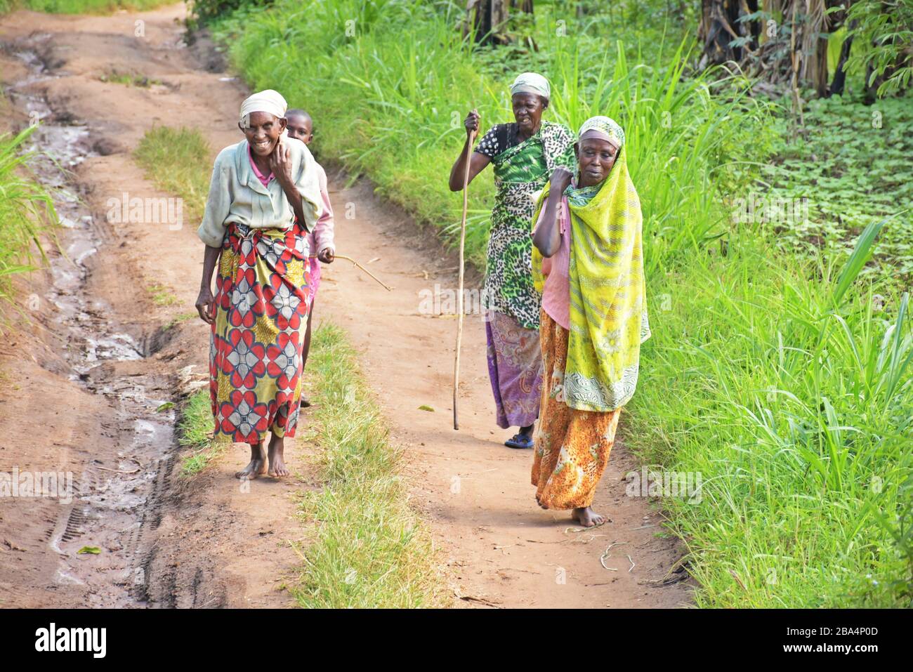 Three African elderly women, two of them barefoot, and a child behind them, walking on narrow dirt road in Rwanda, East Africa Stock Photo