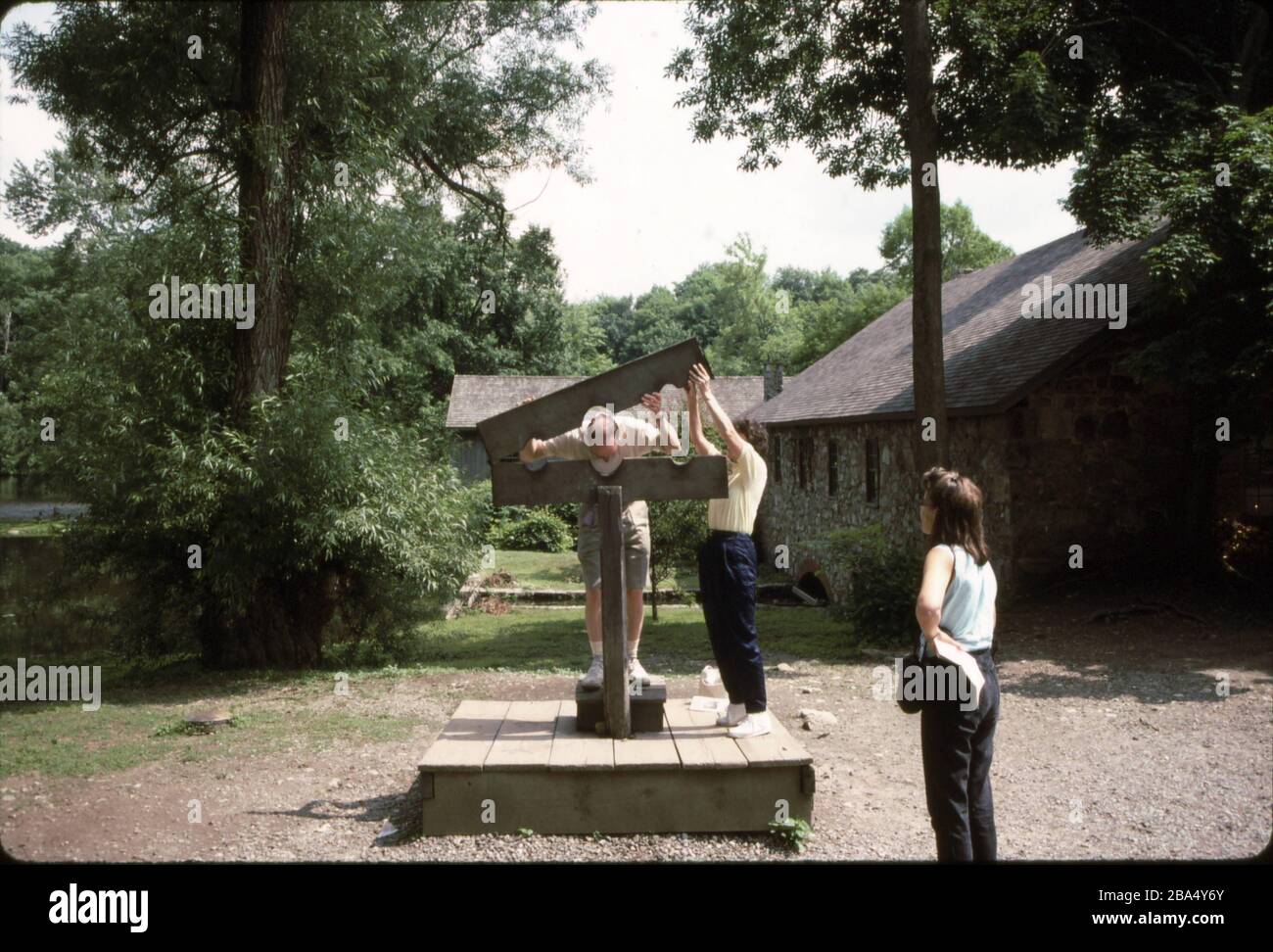 'English: Punishment for less serious crimes at Waterloo Village was meted out in the form of public humiliation in the stocks. In this modern photograph, the unlucky subject is about to be locked in for display and ridicule. Note the gristmill in the immediate background and the sawmill farther in the background towards Waterloo Lake. July 1992; 1 January 2007 (original upload date); Transferred from en.wikipedia to Commons.; WallyFromColumbia at English Wikipedia; ' Stock Photo