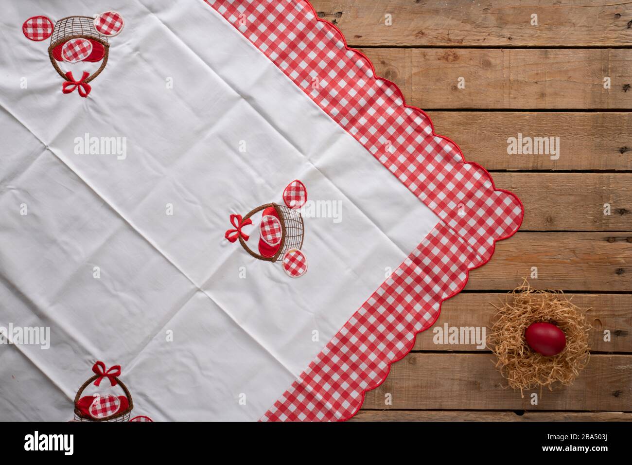Easter tablecloth on a wooden surface with a nest and a red painted egg Stock Photo