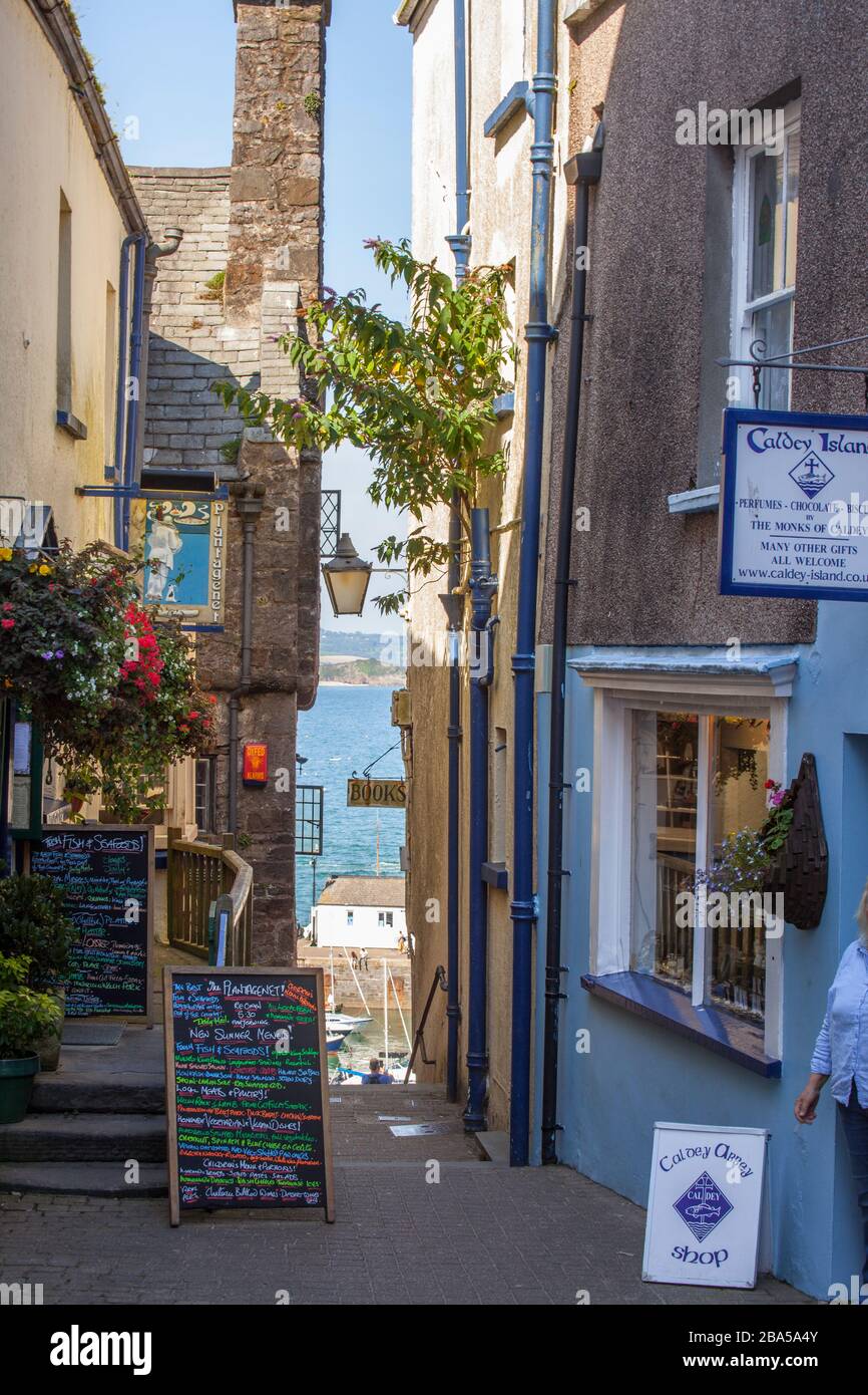 a narrow walkway with a view of the sea. Independent shops on path leading to harbour or seaside. Tenby, Pembrokeshire Stock Photo