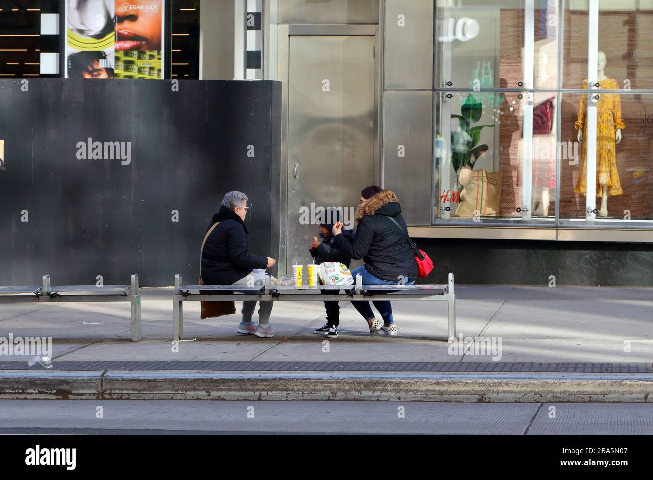 New York, NY. 24th March 2020. A family dines outside on a bench in Manhattan's Upper East Side during the coronavirus COVID-19 pandemic.  An executive order issued by the Governor of New York State has prohibited restaurants and bars from serving customers except for take-out and delivery orders only. Credit: Robert K. Chin. Stock Photo