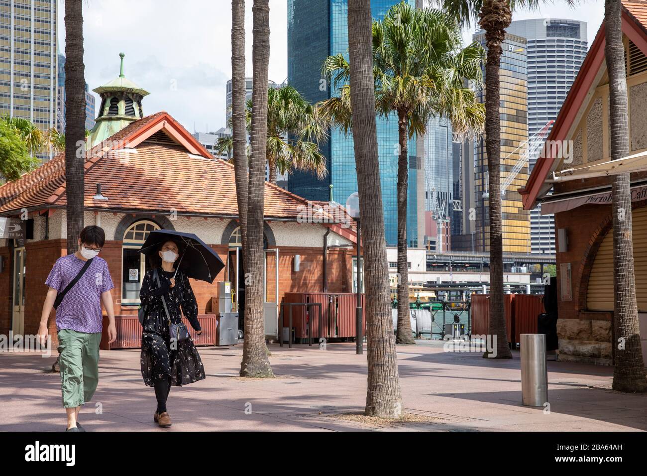 Asian couple wearing face masks walk through an eerily quiet Circular Quay after restaurants are forced to close during coronavirus,Sydney,Australia Stock Photo