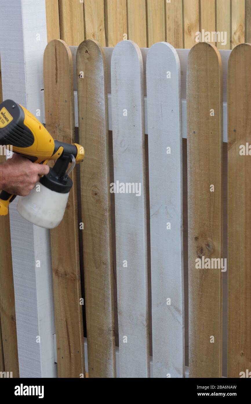 Painter using spray gun to paint bare timber fence using white