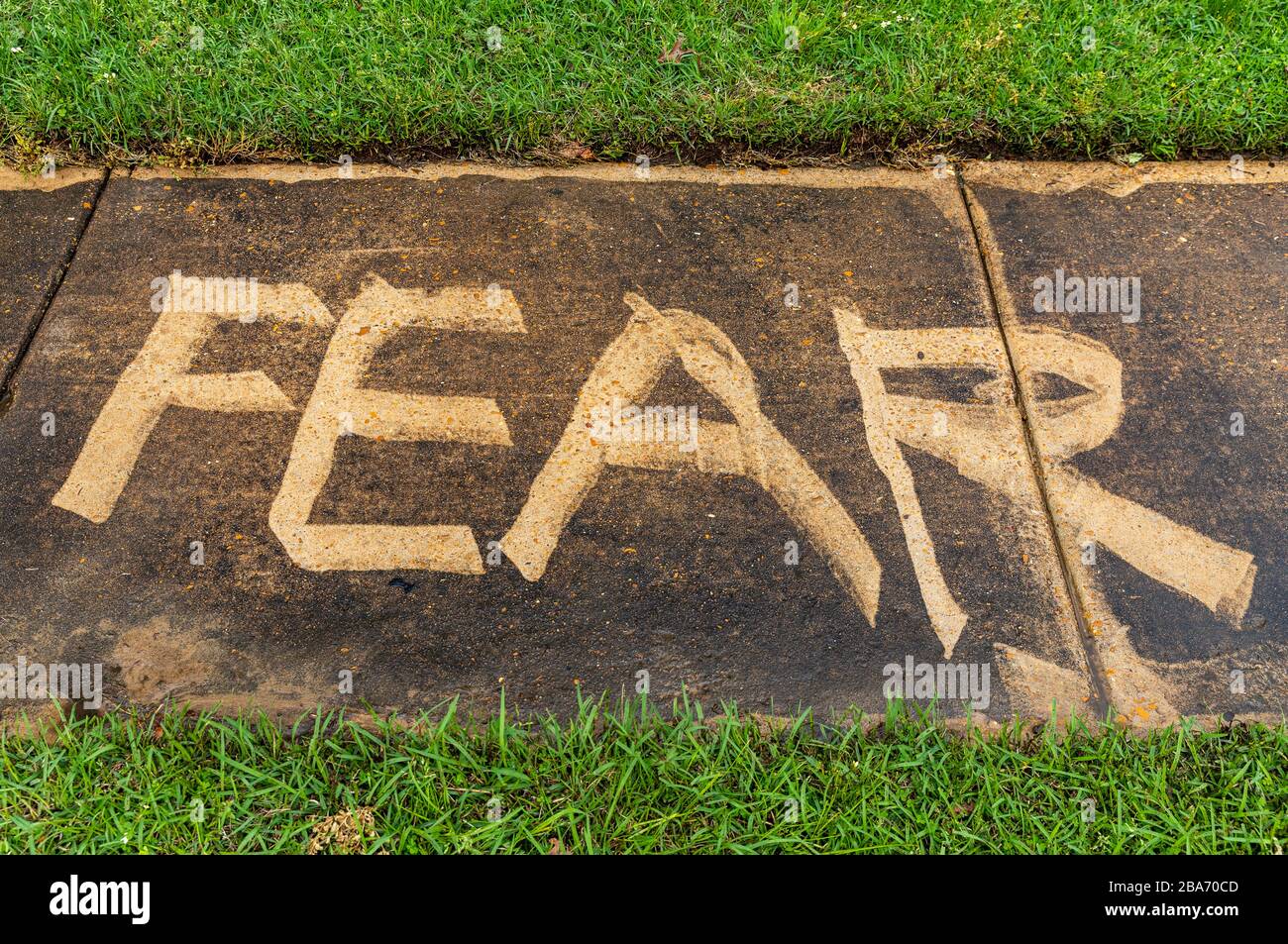 The word 'Fear' pressure on a sidewalk, with grass and copy space Stock Photo