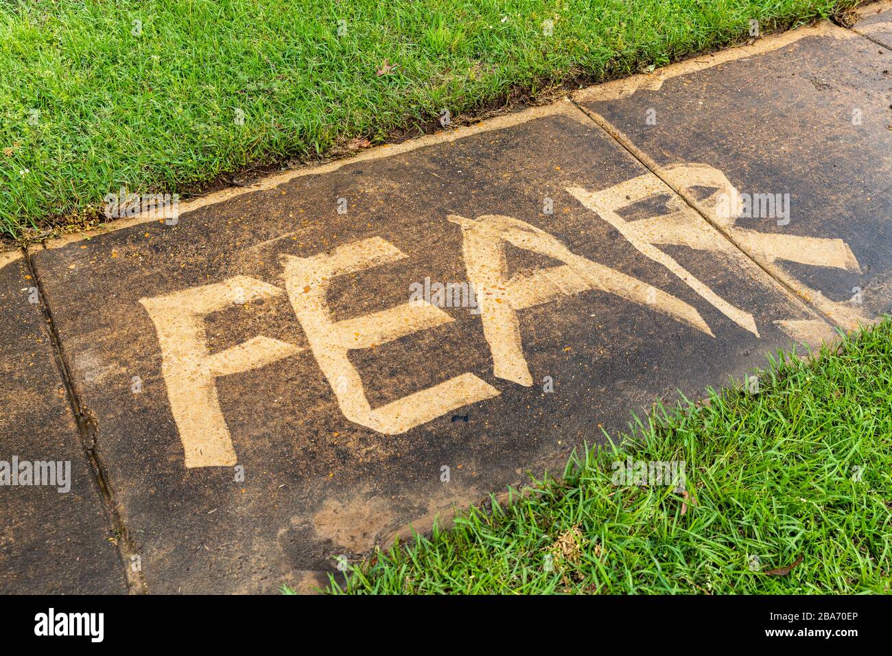 The word 'Fear' pressure on a sidewalk, with grass and copy space Stock Photo
