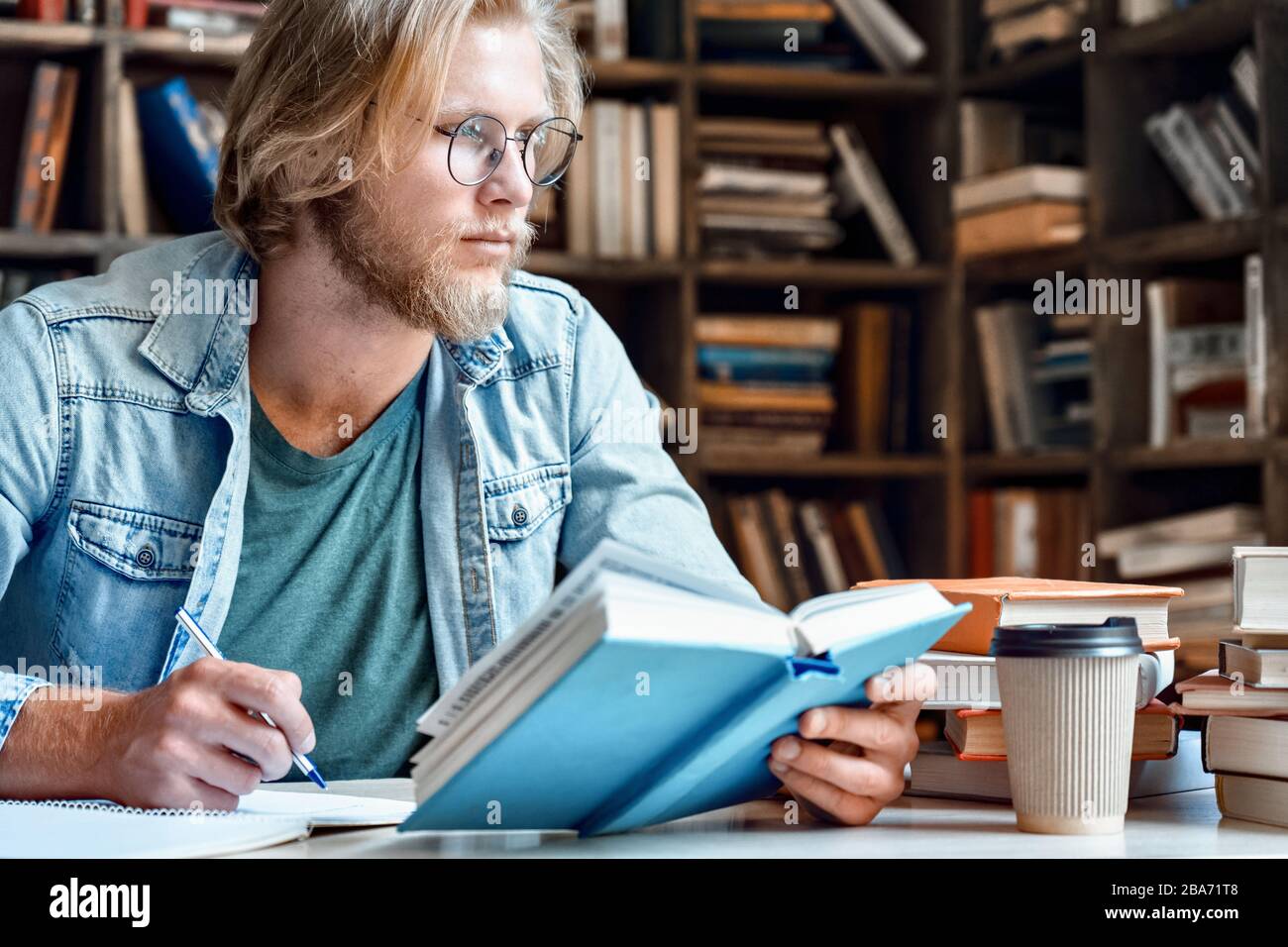 Young student in library at desk look away handwrite in notebook. Stock Photo