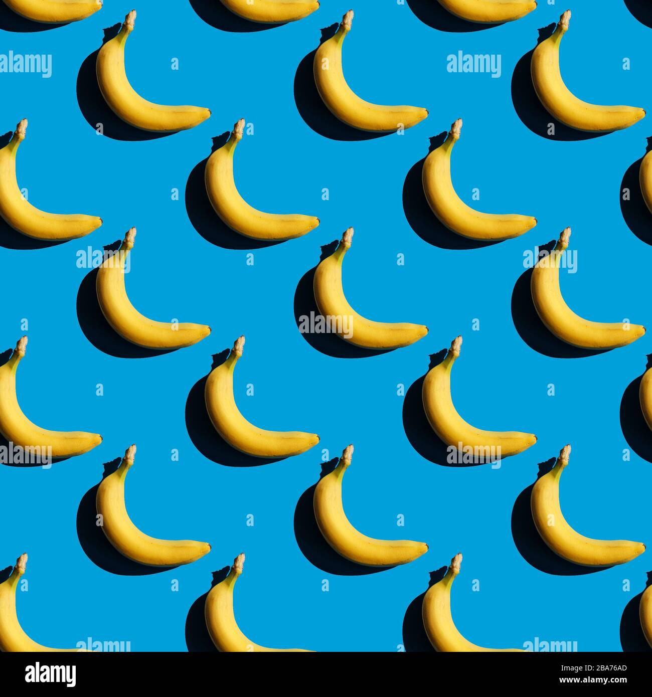 Seamless bananas pattern. Creative yellow food on blue background. Fresh season fruit texture with strong shadows Stock Photo