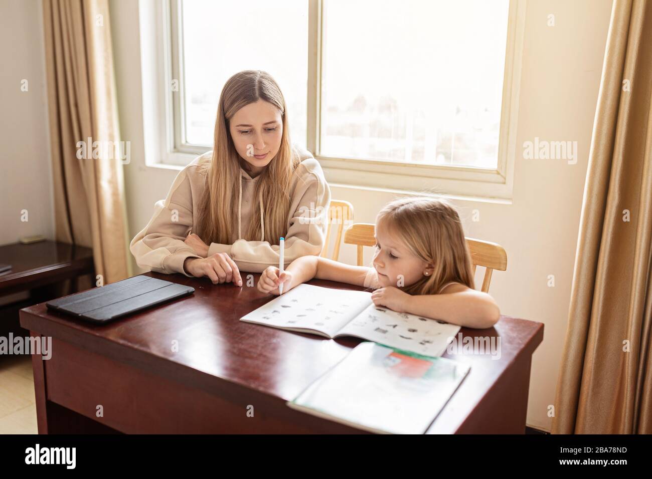 Mother helping her daughter making school homework at home. Learning at home, online learning, self quarantine, Home schooling and concept of COVID-19 Stock Photo