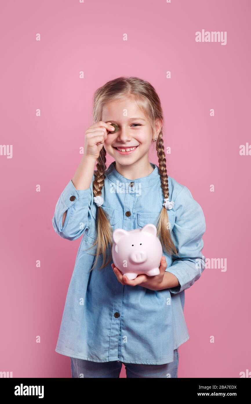 Cute little girl putting coin into piggy bank on pink background Stock ...