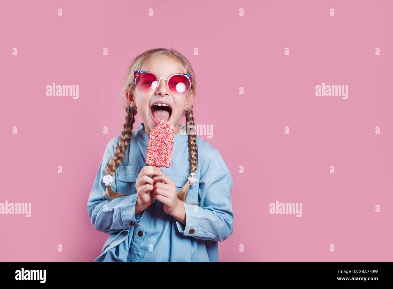 little cheerful girl in sunglasses with ice cream on pink background Stock Photo