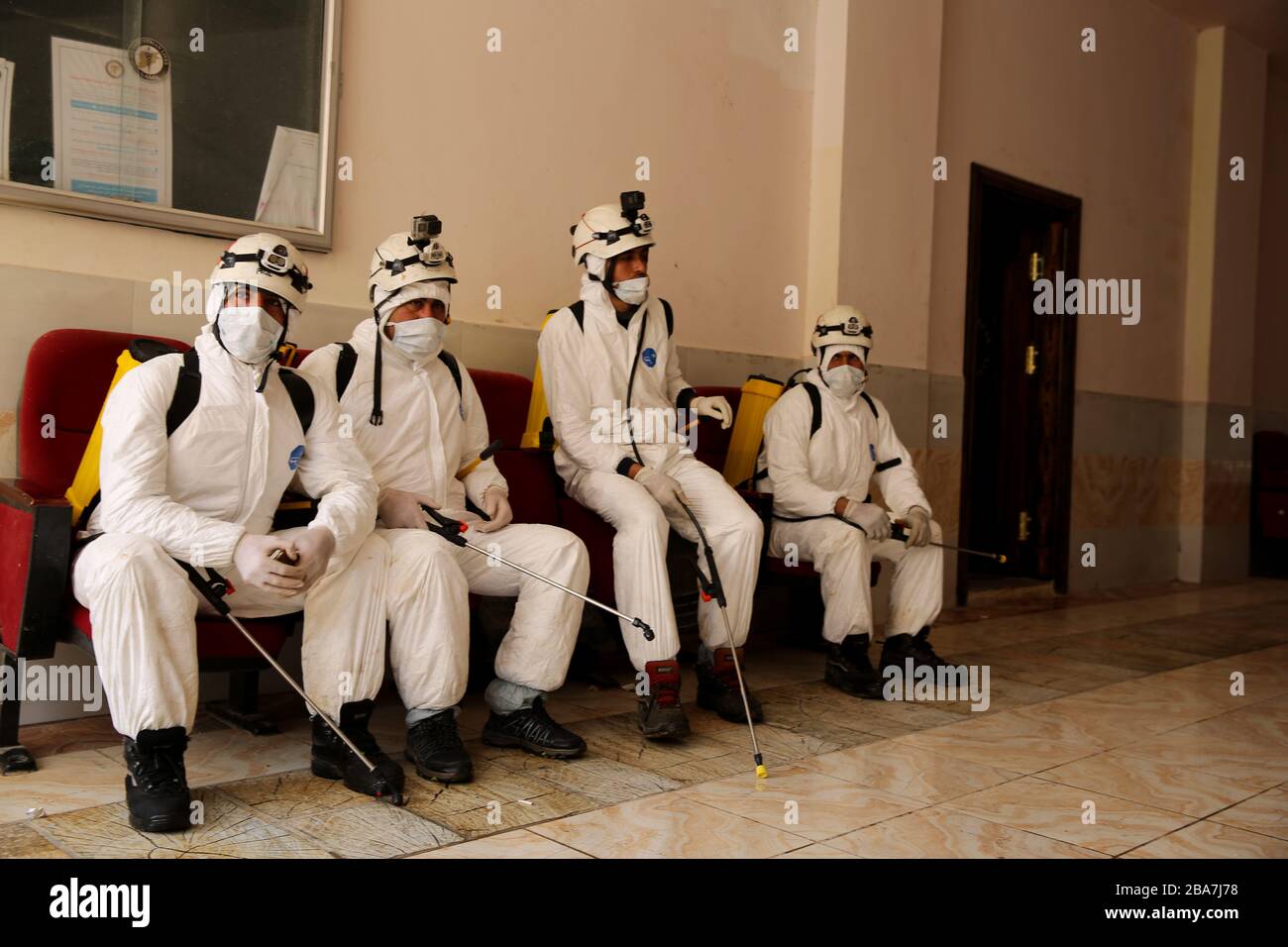 March 24, 2020: Aleppo, Syria. 24 March 2020. Members of the Syrian Civil Defence clad in protective gear spray with disinfectant the premises of a medical clinic in the town of Atarib, in the western Aleppo countryside, as part of preventive measures against the spread of the Coronavirus in the area. Although in the rebel-held northwest part of Syria no Covid-19 cases have been confirmed, some preventive measures are now in place to contain a possible epidemic in the warn-torn country. The Syrian government is also applying tight measures after the first case of Covid 19 in the country was an Stock Photo