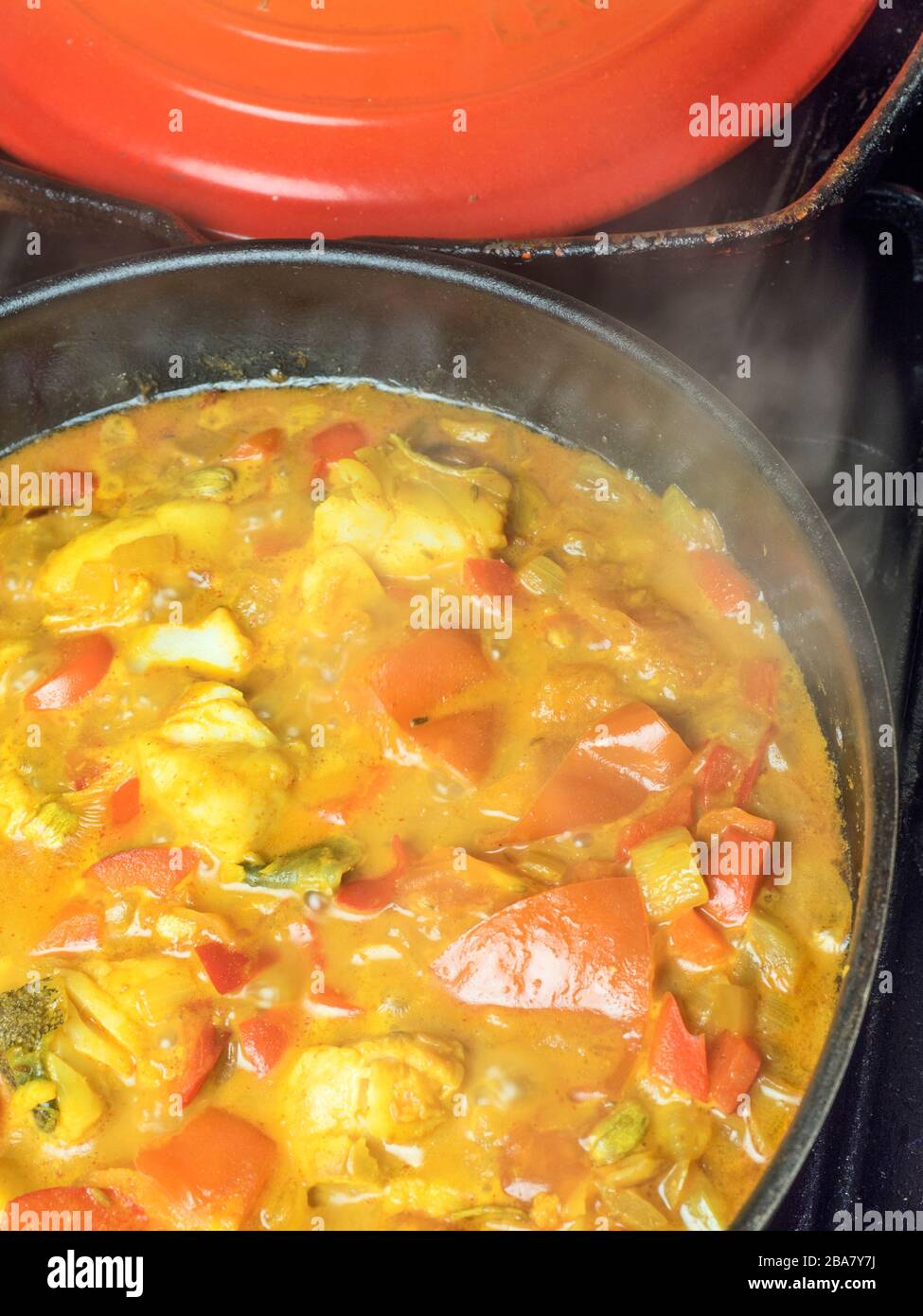 Curry made with white fish red peppers and tomatoes simmering in a pan on a hob Stock Photo