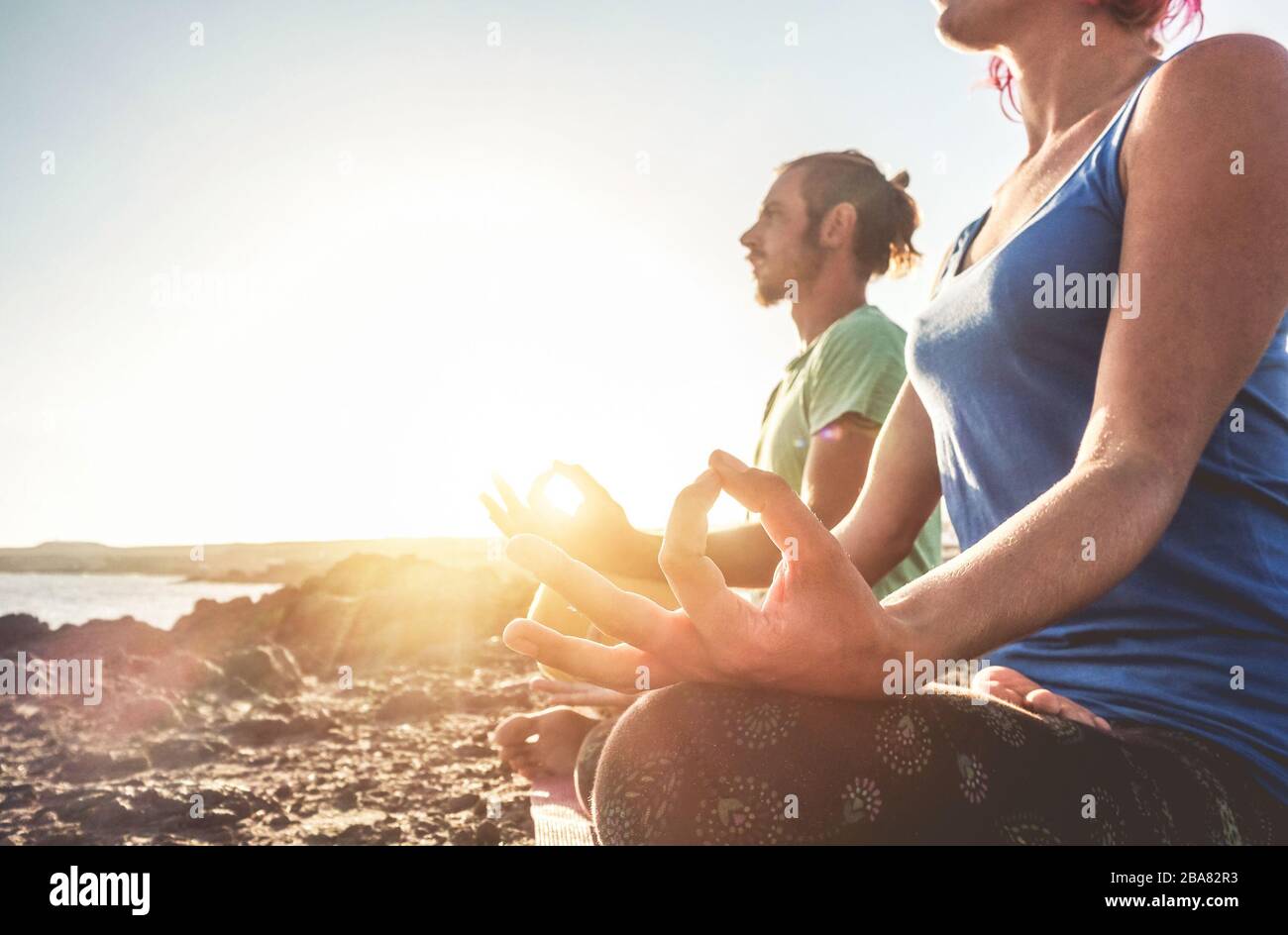 Couple doing yoga outdoor at sunrise in nature - Woman and man meditating together at morning time - Concept of fitness exercise for healthy lifestyle Stock Photo