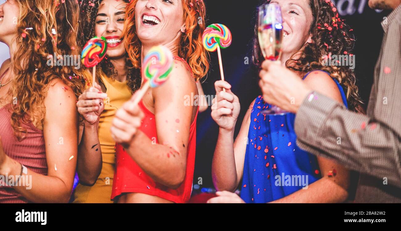 Young friends drinking champagne while dancing inside disco club - Happy people having fun eating candy lollipops at night party - Holidays and nightl Stock Photo