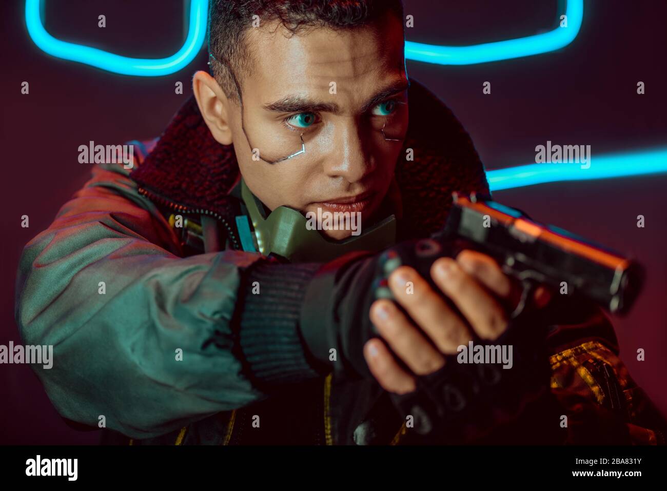 selective focus of dangerous bi-racial cyberpunk player with gun on black with neon lighting Stock Photo