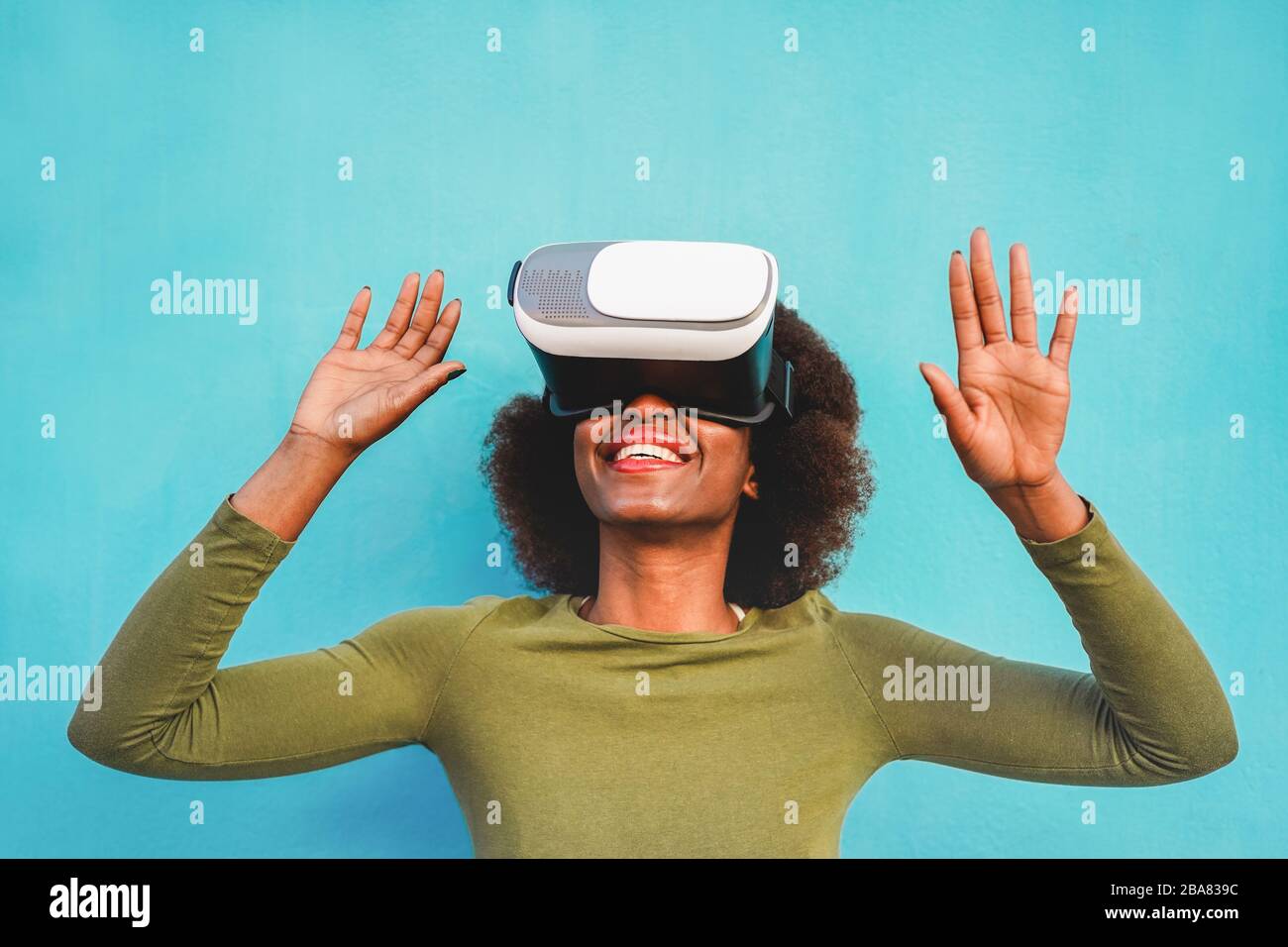 Young woman using virtual reality headset with blue wall in background ...