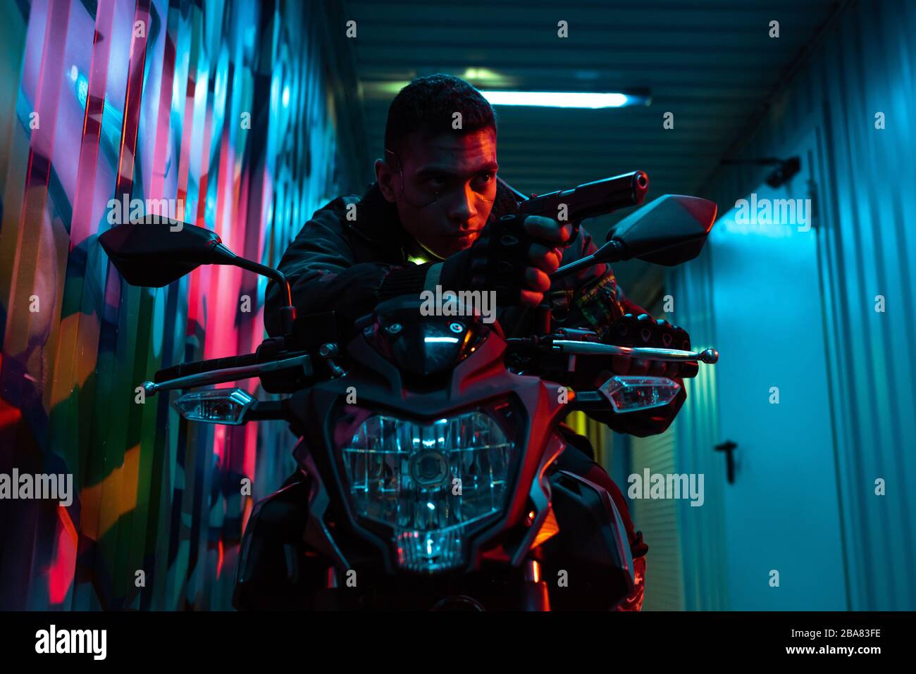 bi-racial cyberpunk player on motorcycle aiming gun on street with graffiti Stock Photo
