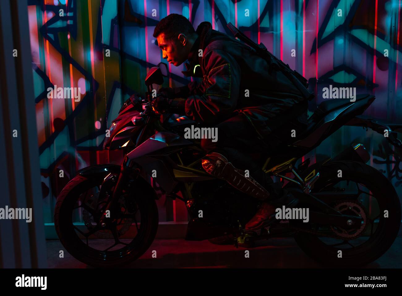 profile of mixed race cyberpunk player riding motorcycle on street with graffiti Stock Photo