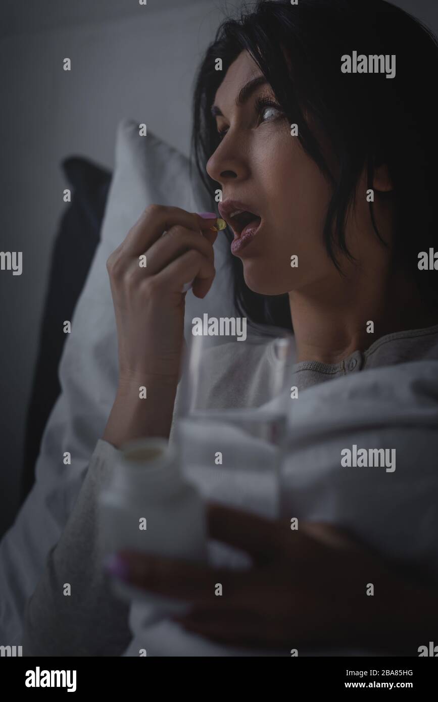selective focus of awake woman holding glass of water while taking sleeping pill Stock Photo