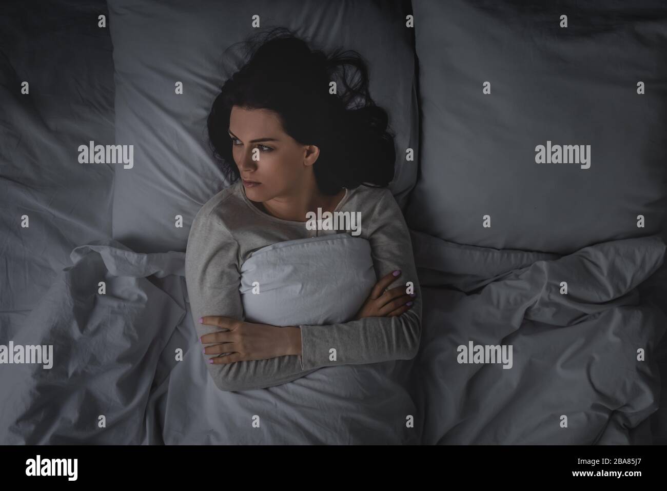 top view of woman with sleep disorder and crossed arms lying in bedroom