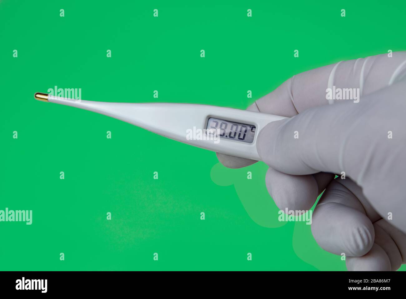 Hand with a Thermometer on Green background. The thermometer shows a temperature of 39 Celsius. Coronavirus 2019-nCoV. Corona virus outbreaking. Stock Photo