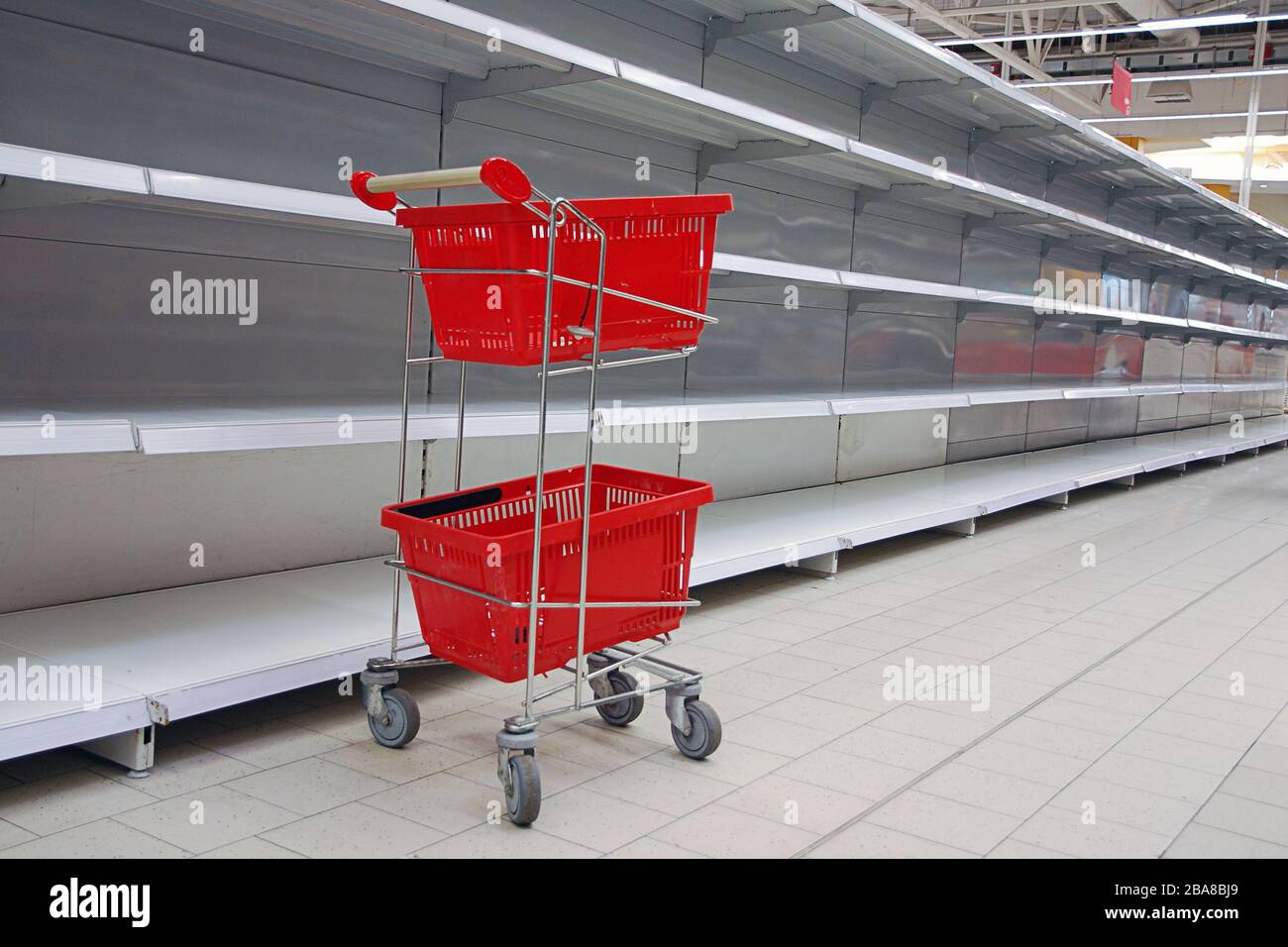 Shopping trolley with empty baskets by empty shelves in supermarket Stock Photo