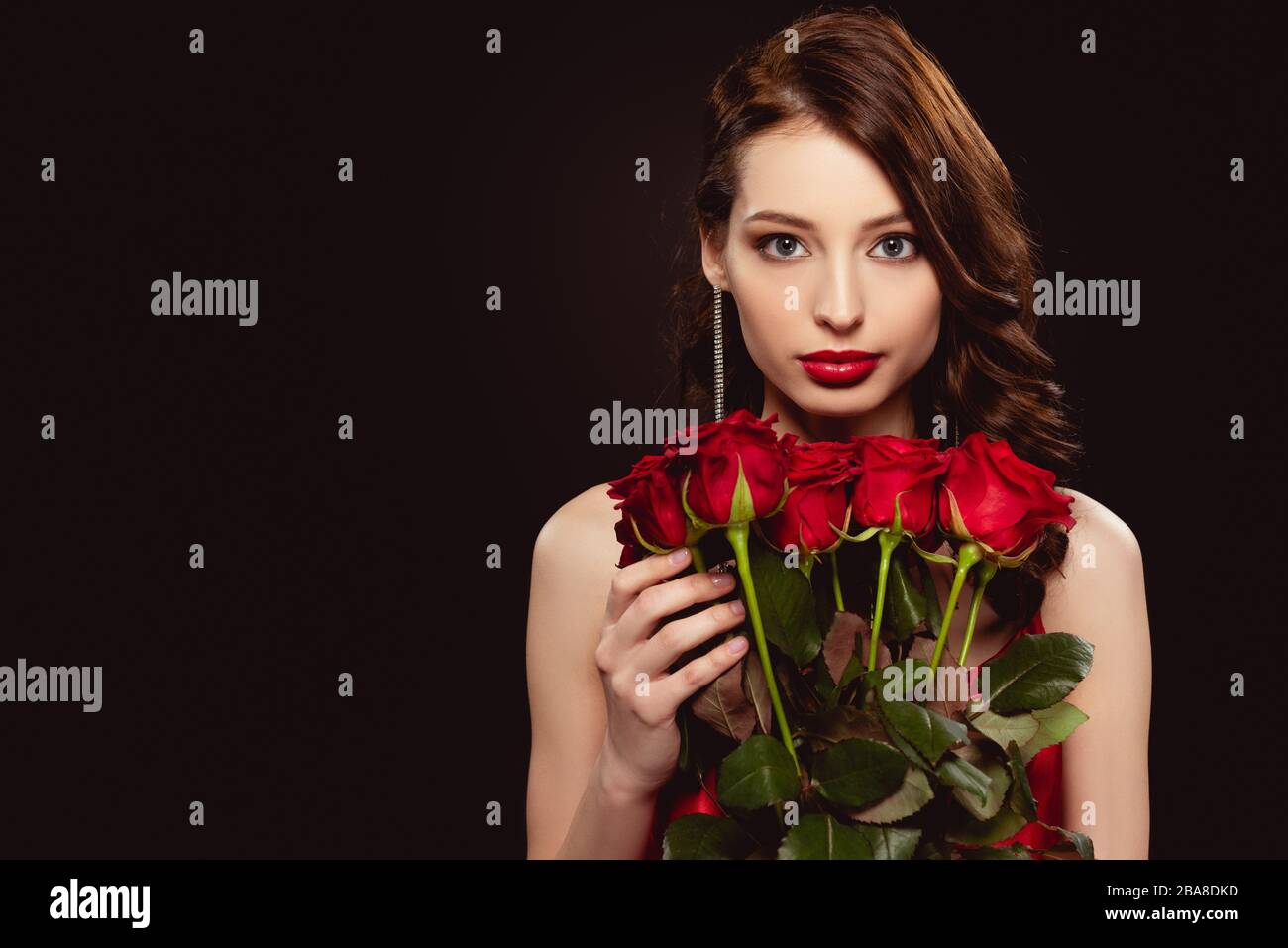 Attractive young woman holding bouquet of red roses and looking at ...