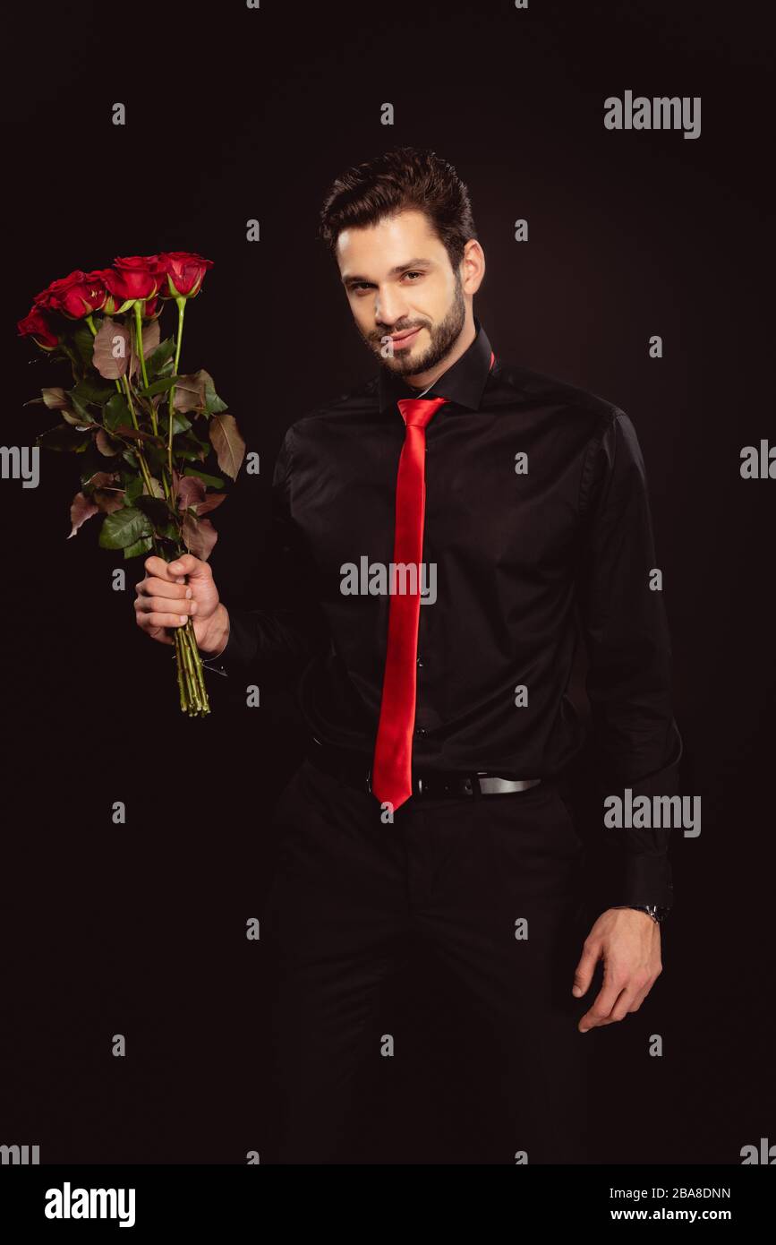 Handsome man in formal wear and red tie looking at camera and holding  bouquet of roses isolated on black Stock Photo - Alamy