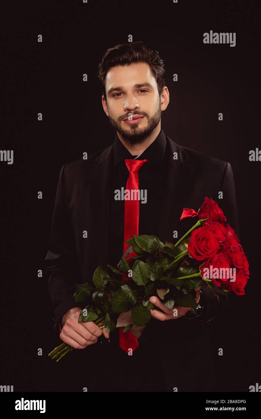 Handsome man in suit holding bouquet of red roses and looking at camera ...