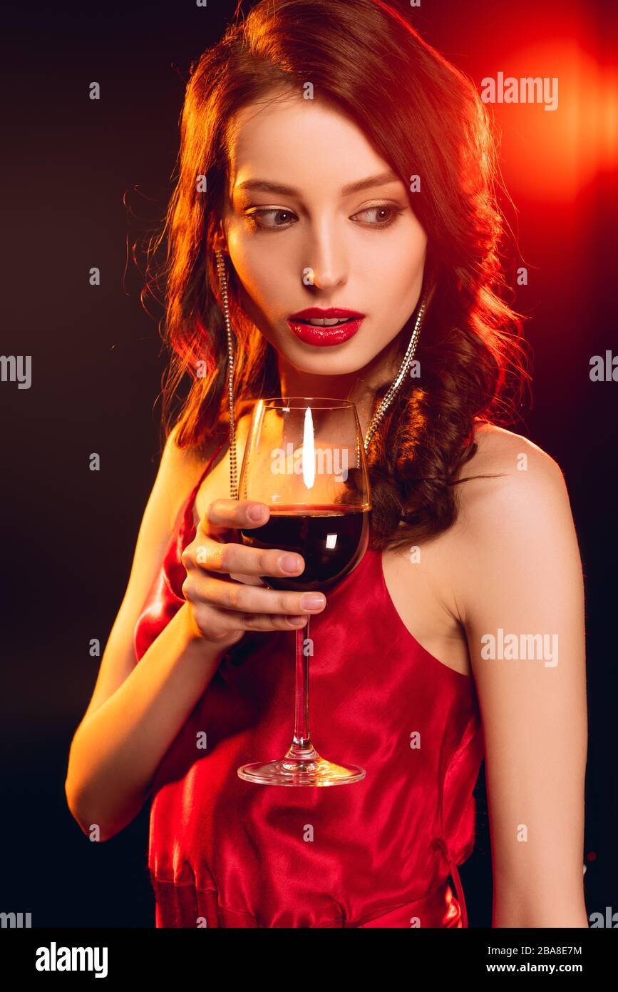 Beautiful woman in red dress holding glass of wine on black background ...
