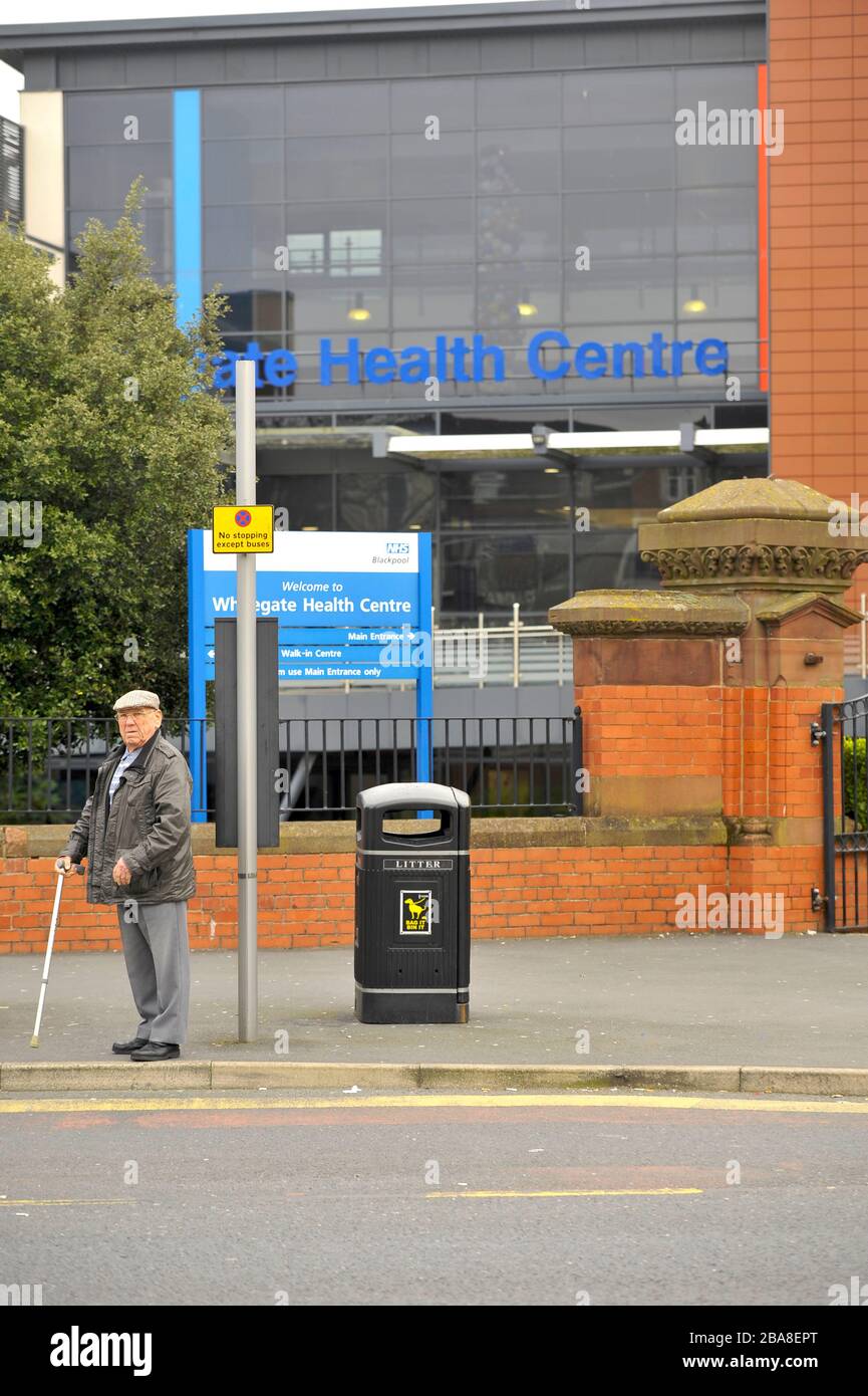Senior man at bus stop with walking stick stood outside a health centre in Blackpool Stock Photo