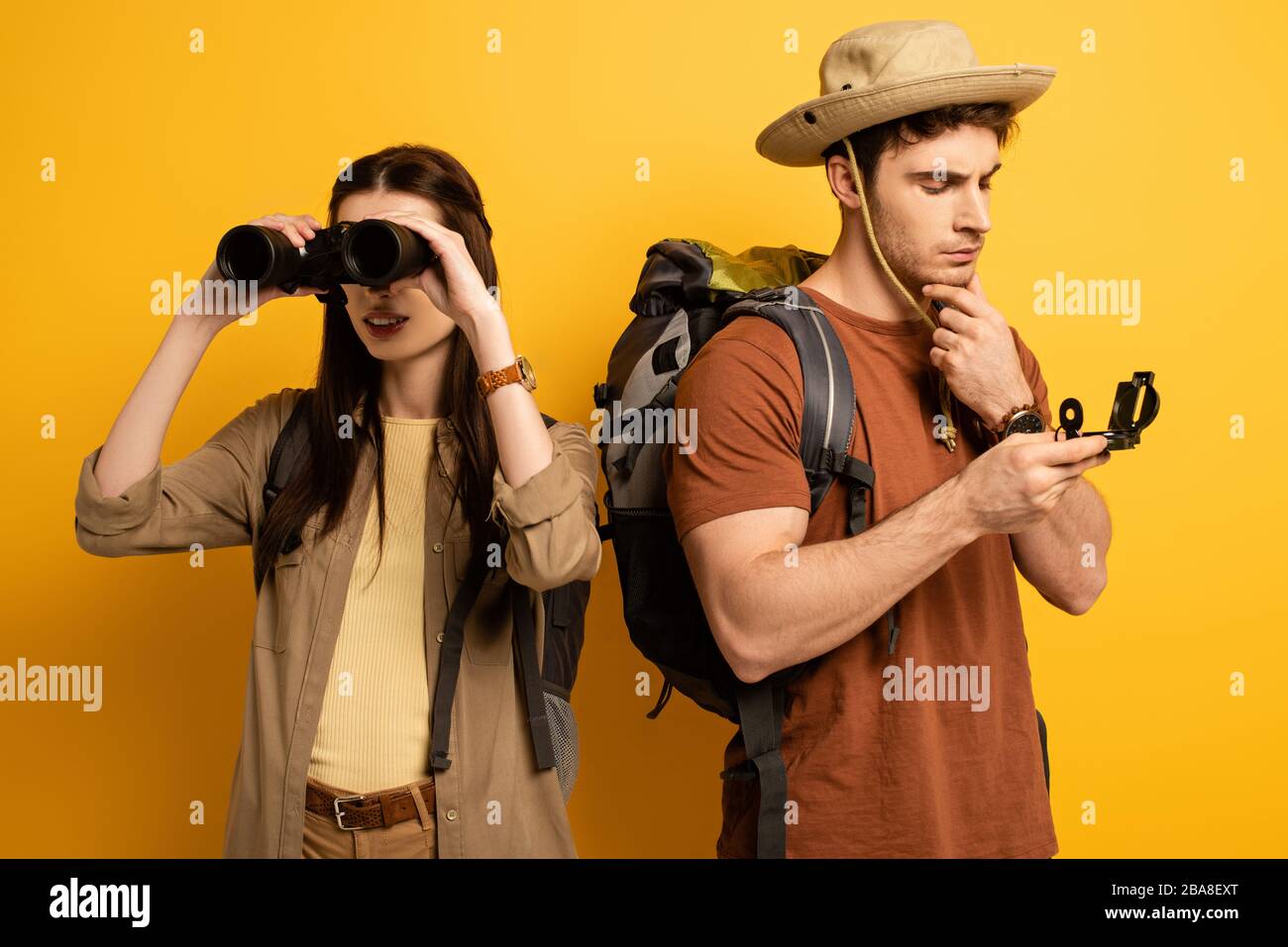 couple of tourists with backpacks and binoculars looking at compass on yellow Stock Photo Alamy