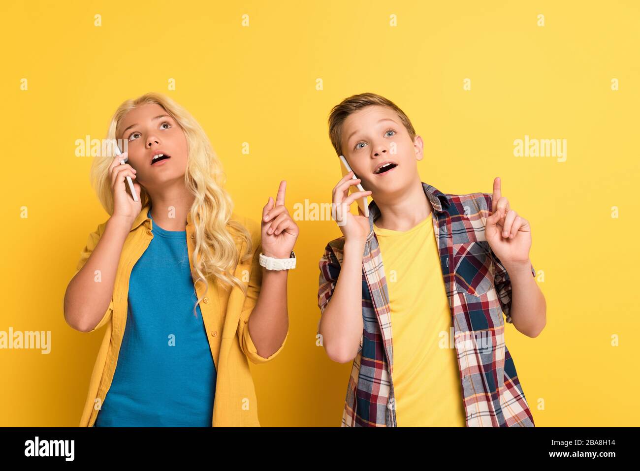 dreamy kids showing idea gesture and talking on smartphones on yellow background Stock Photo