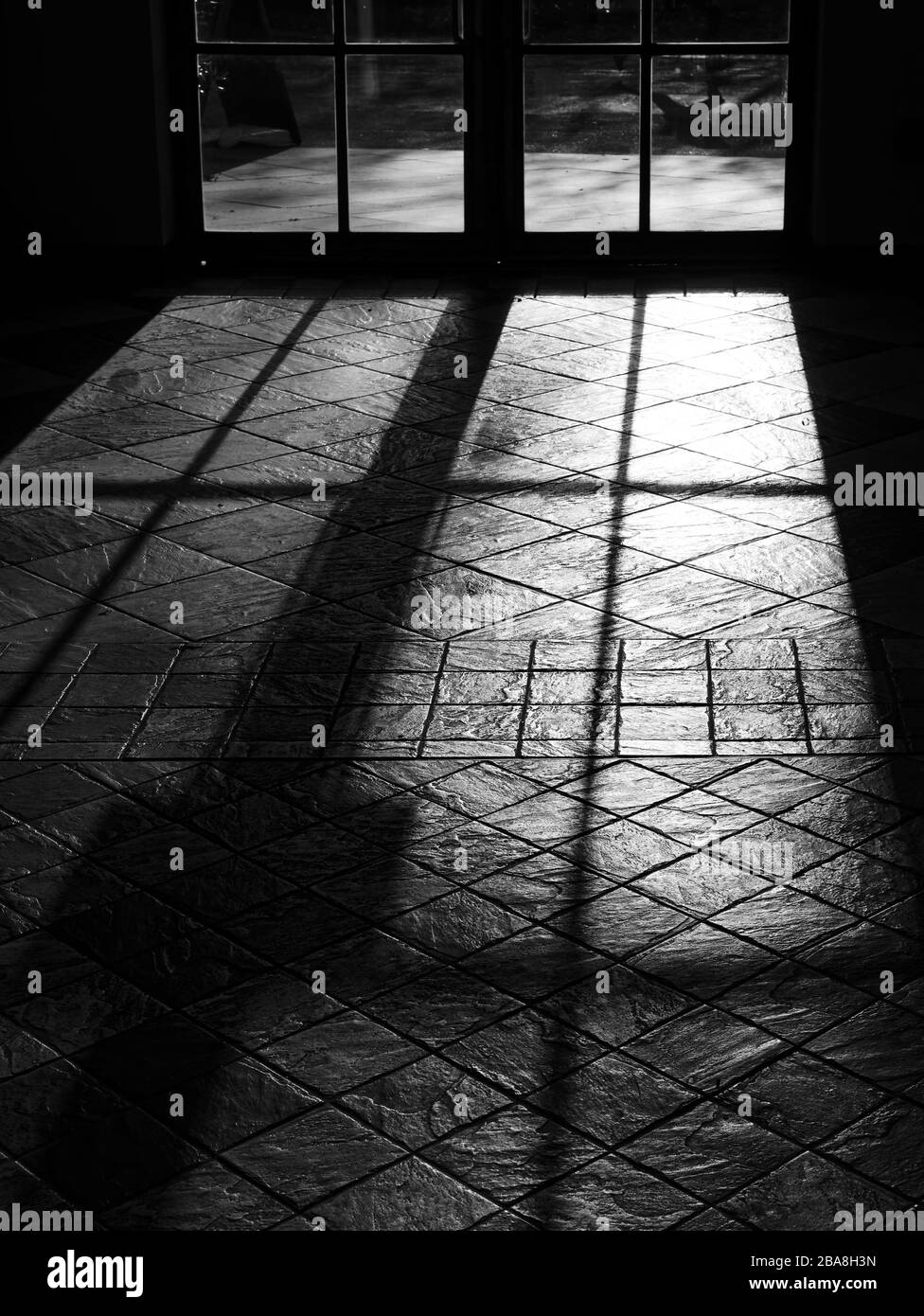 French windows casting dramatic light rays and shadow on the floor tiles. Black and white image. Stock Photo